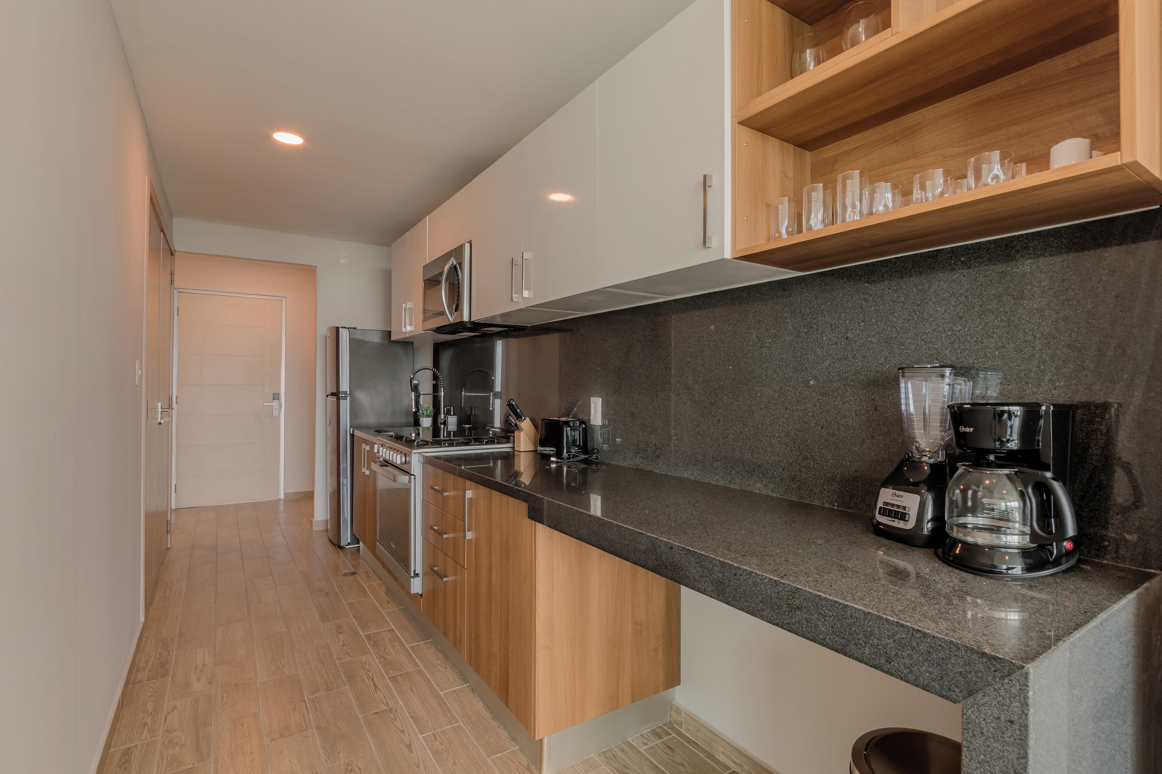 A modern kitchen with wooden cabinets, a granite countertop, a refrigerator, a coffee maker, and a blender.