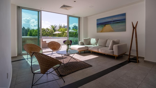 Een moderne woonkamer met een bank, twee rieten fauteuils, een salontafel en een schilderij van een strandgezicht.