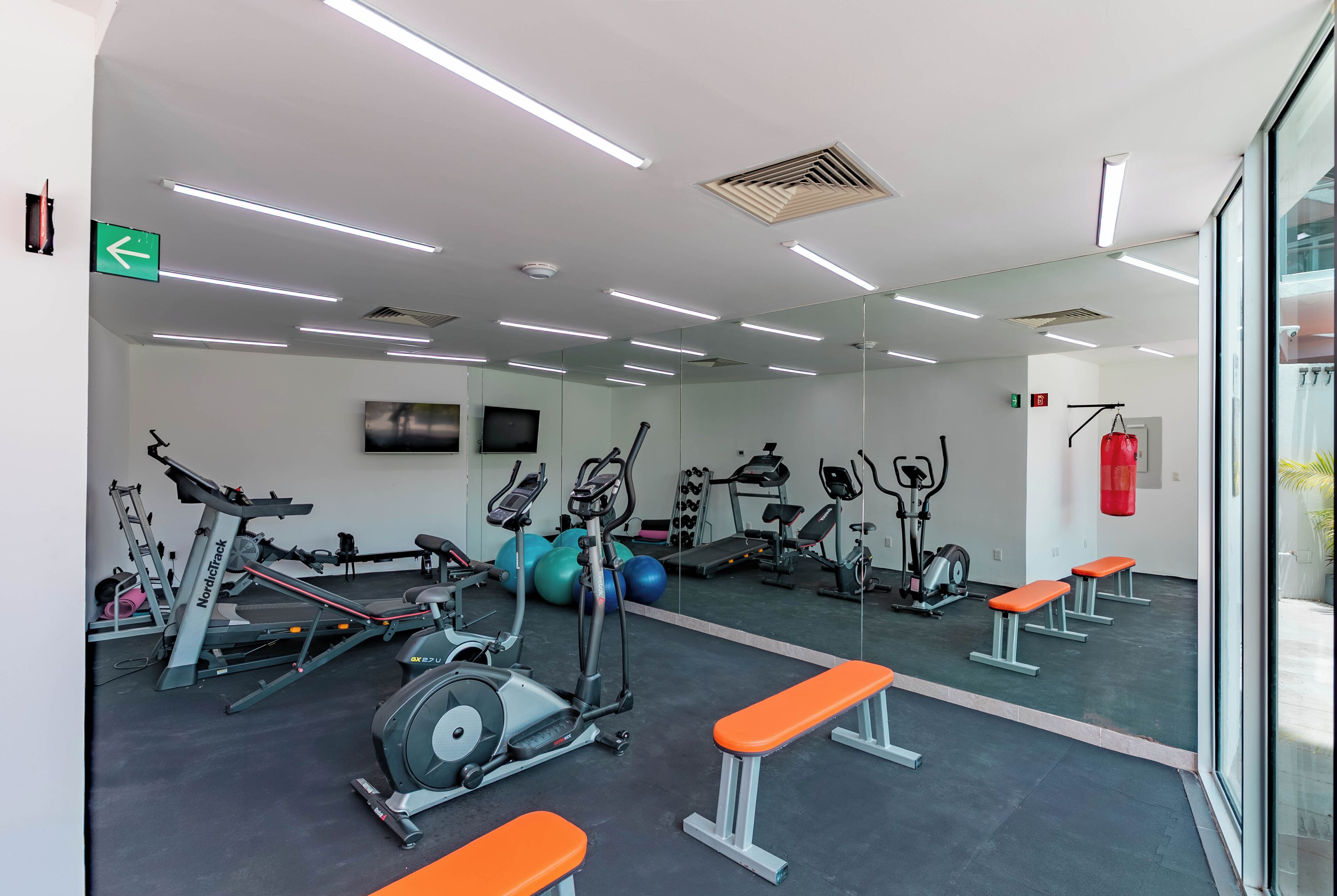 Un gimnasio con equipo de ejercicio, bancos y un espejo grande.