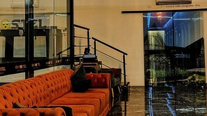 Un hall d’entrée moderne avec un grand lustre illuminé, un canapé orange moelleux et un sol en marbre poli.