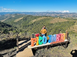A wooden sign with colorful letters spelling "PICOMBRIA" and "QUADRAMA" on a wooden platform, set against a backdrop of a mountainous landscape. - On Hotel campos do Jordao centro Capivari e passeio quadriciclo (Campos do Jordão)