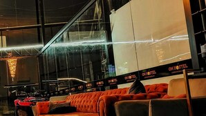Un hall d’hôtel moderne avec un grand canapé rouge, un ascenseur en verre et un lustre.