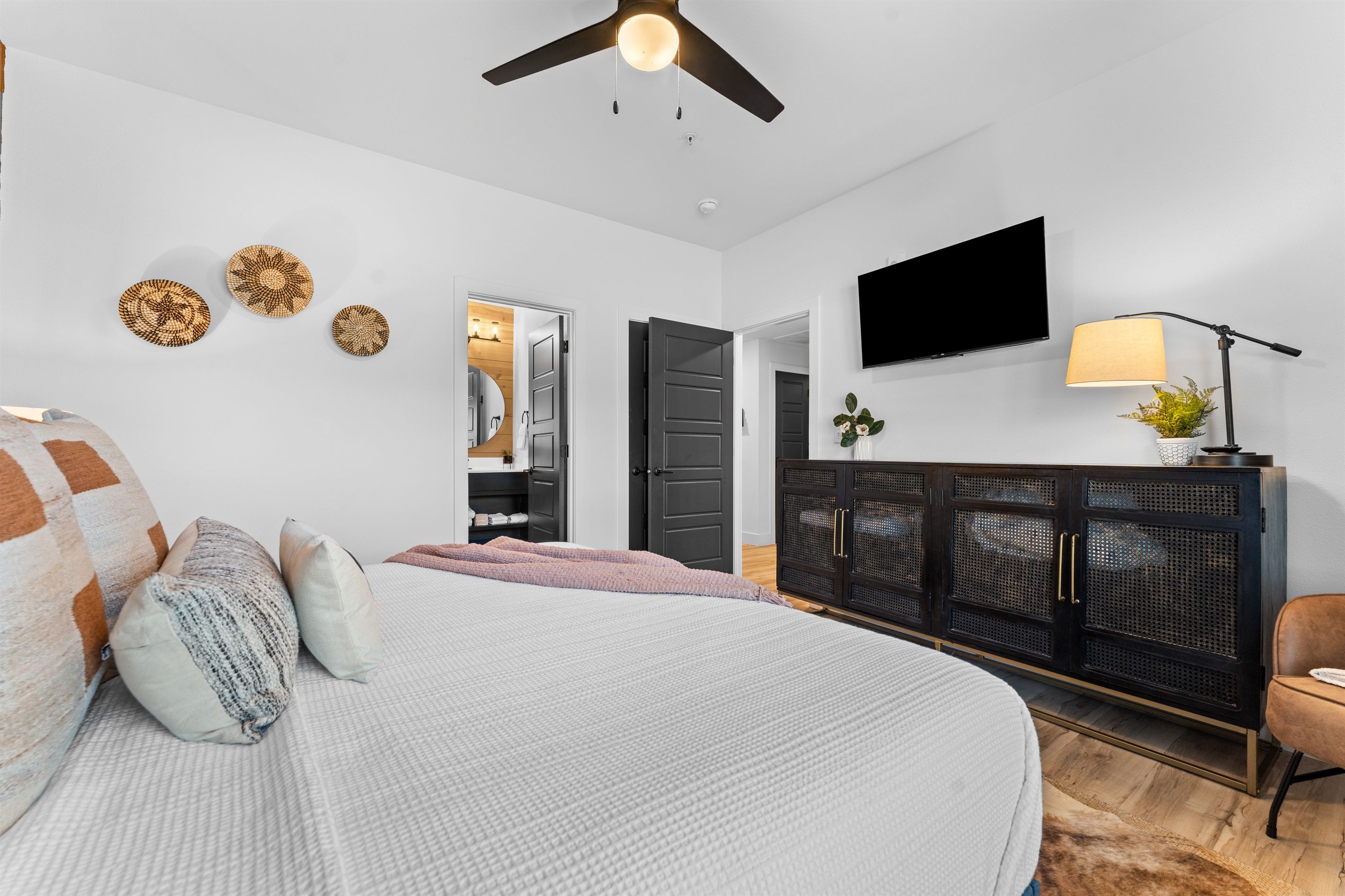 A bedroom with a bed, a ceiling fan, a TV, a cabinet, and a plant.