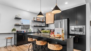 A modern kitchen with black cabinets, stainless steel appliances, wooden stools, and pendant lighting. - Solid Rock Lodge >Lake View >Hot Tub >Indoor Pool > Near Big Cedar&Thunder Ridge (Hollister)