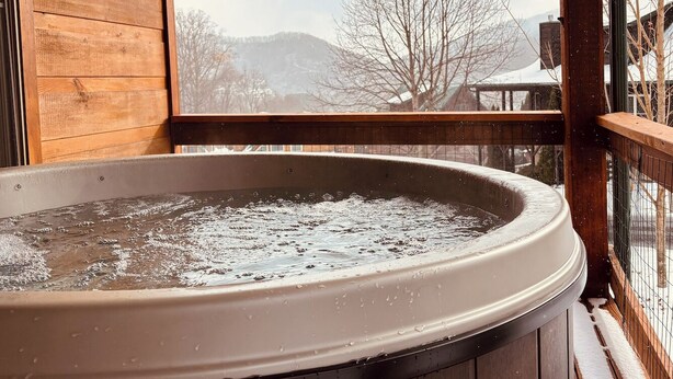 A hot tub in a wooden cabin with a view of a snowy landscape.