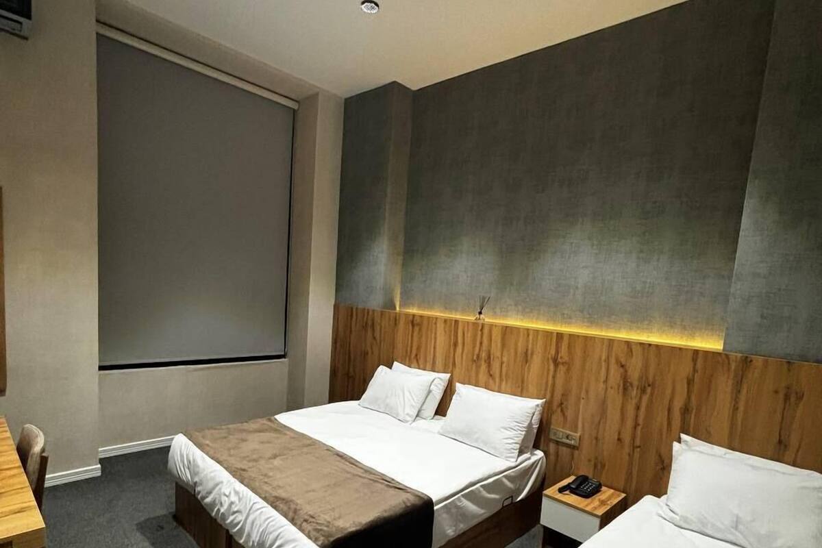 A modern hotel room with a large bed, a smaller bed, a desk, and a projector screen.