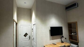 A compact room with a desk, chair, TV, and built-in shelving.