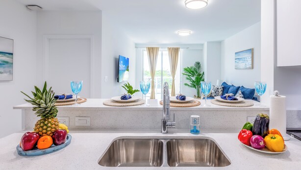 A modern kitchen with a stainless steel sink, a fruit bowl, and a plate of vegetables. - Modern 1BR Apt in Hollywood, FL – 5 Mins to Beach, W/ Pool, Gym, & Free Parking (Hollywood)