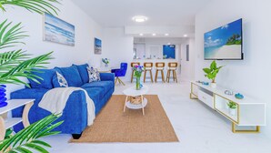 A modern living room with a blue sofa, a coffee table, and a TV mounted on the wall. - Modern 1BR Apt in Hollywood, FL – 5 Mins to Beach, W/ Pool, Gym, & Free Parking (Hollywood)