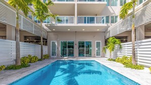 A modern building with a swimming pool surrounded by palm trees and a white fence. - Modern 1BR Apt in Hollywood, FL – 5 Mins to Beach, W/ Pool, Gym, & Free Parking (Hollywood)