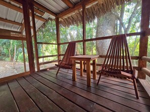 A wooden deck with a table and two chairs, surrounded by a mesh fence and large windows. - Cotton Tree Cabin in Hopkins (Hopkins Village)
