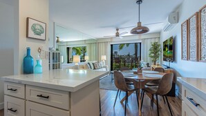 A modern kitchen with a central island, dining area with chairs, and a large window with a view. - Welcome to Mavi Bay, luxury ocean view condo,by Kamaole II beach newly renovated (Kihei)