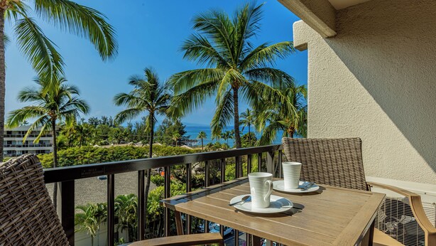 A wooden table with white cups and saucers, wicker chairs, and a view of the ocean and palm trees. - Welcome to Mavi Bay, luxury ocean view condo,by Kamaole II beach newly renovated (Kihei)