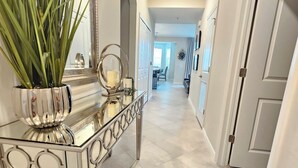 A hallway with a mirrored console table, a potted plant, and a door leading to another room. -  18-hole Golf Course Condo. Two bedrooms-Two bath with amazing views  (Ave Maria)