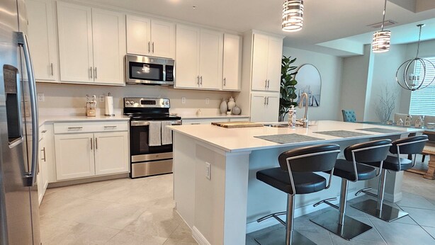 A modern kitchen with white cabinets, stainless steel appliances, and a central island with bar stools. -  18-hole Golf Course Condo. Two bedrooms-Two bath with amazing views  (Ave Maria)