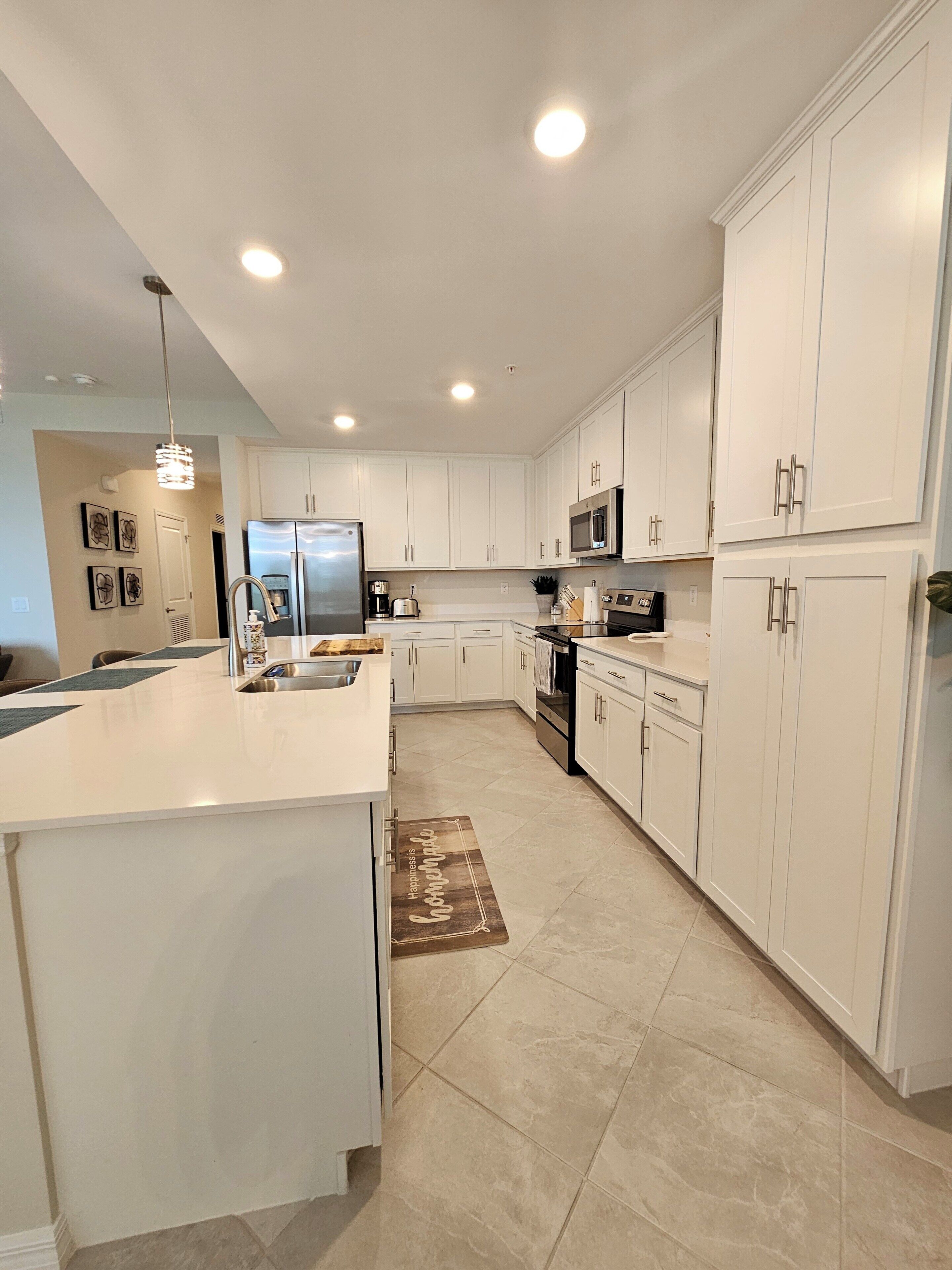 A modern kitchen with white cabinetry, a stainless steel refrigerator, a microwave, and a large island with a sink.