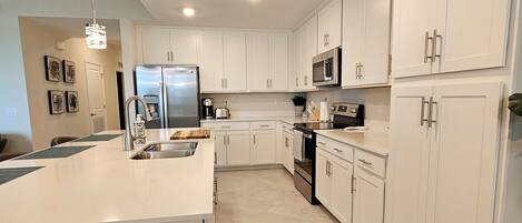 A modern kitchen with white cabinetry, a stainless steel refrigerator, a microwave, and a large island with a sink.