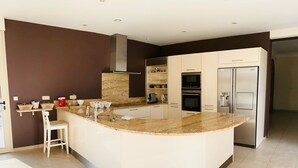 Une cuisine moderne dotée d’un îlot central, de meubles blancs, d’appareils électroménagers en acier inoxydable et d’un mur d’accent de couleur marron.