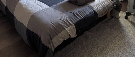 Ein Schlafzimmer mit Holzkopfende, einem Bett mit Patchworkdecke, einem Nachttisch, einem Heizkörper und einem Fenster mit Vorhängen.