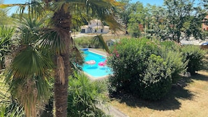 Une piscine entourée d’une végétation luxuriante et de palmiers, avec un bâtiment en arrière-plan.