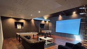 Un salon moderne équipé d’une table de billard, d’un canapé, d’une table basse et d’un écran de projection.