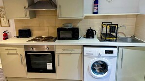 Une cuisine compacte équipée d’une cuisinière, d’un four à micro-ondes, d’un grille-pain, d’une bouilloire et d’un lave-linge.