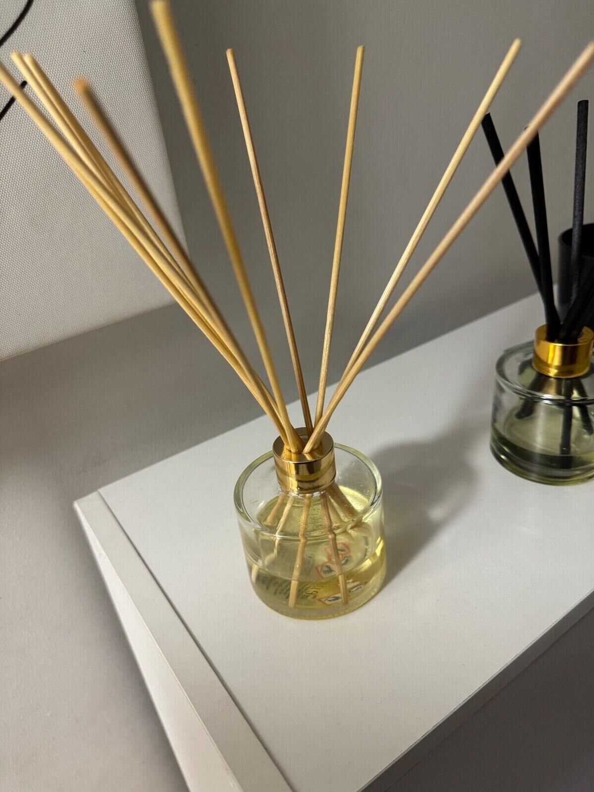 Un difusor de vidrio con palitos de juncos sobre un estante blanco.