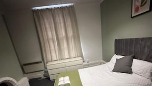 Un lit bien fait, avec une couverture verte, une tête de lit et une table de chevet sur laquelle est posée une serviette.