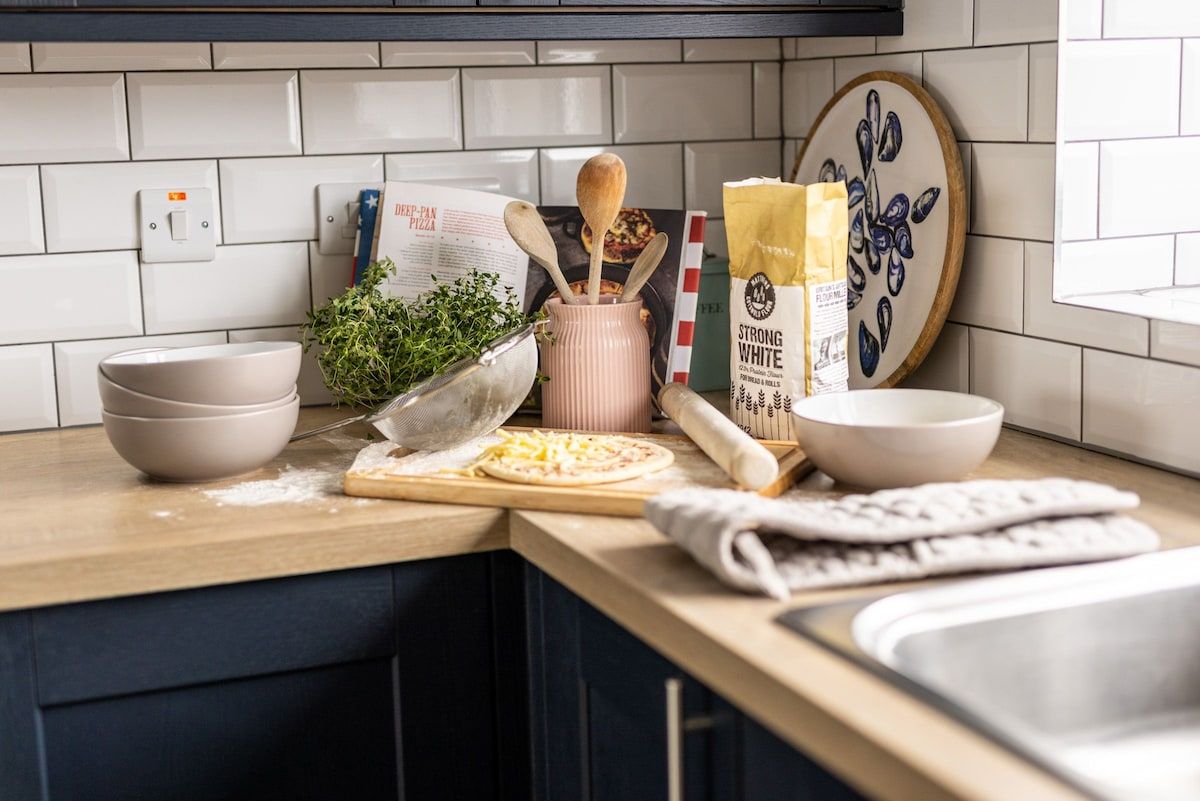 Un plan de travail de cuisine avec une pizza, des bols, un rouleau à pâtisserie et un livre de recettes.