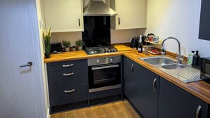 Une cuisine compacte équipée d’une cuisinière à gaz, d’un four et d’un évier, de plans de travail en bois et de meubles de rangement aux couleurs sombres.