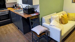 Une cuisine compacte équipée d’un four à micro-ondes, d’un grille-pain et d’un évier. On y trouve un petit tabouret et un canapé blanc avec des coussins.