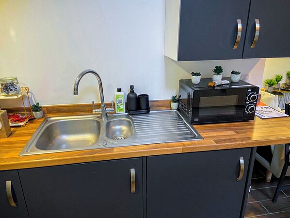 A modern kitchen with a stainless steel sink, a black microwave, and a wooden countertop.