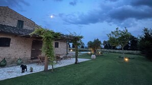 Un bâtiment rustique en pierre, doté d’un toit en tuiles, d’une pergola en bois recouverte de lierre et d’une terrasse pavée aménagée avec du mobilier d’extérieur.
