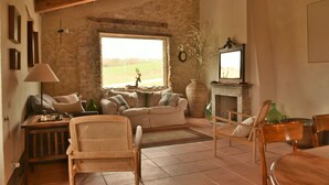 Un salon rustique avec un mur en pierre, un canapé, une chaise en bois, une cheminée et une grande fenêtre.