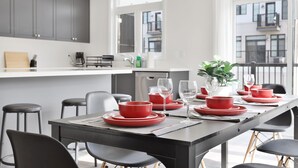 Una cocina moderna con armarios grises, encimera blanca y una zona de comedor con vajilla roja.