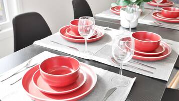 Una mesa de comedor dispuesta con platos, tazones y copas de vino rojos, sobre individuales grises.