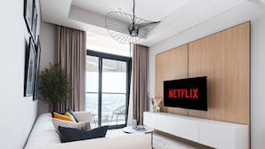Ein modernes Wohnzimmer mit einem großen Flachbildfernseher an einer Holzwand, einer Couch mit Kissen, einem Couchtisch und einer Topfpflanze.