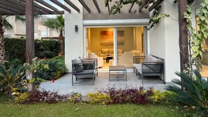 Un patio couvert avec des sièges d’extérieur, une pergola et une vue sur un espace intérieur moderne.