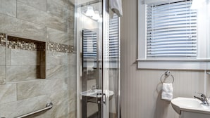 Un baño con cabina de ducha de vidrio, un lavabo y una ventana con persianas.