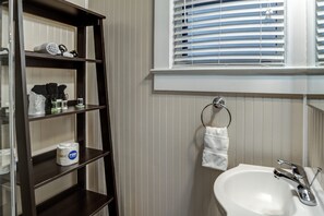 Une salle de bain avec un lavabo blanc, un porte-serviettes et une étagère contenant des articles de toilette.