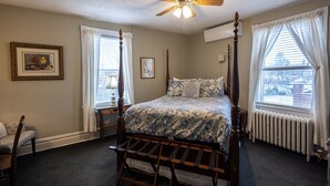 Une chambre à coucher avec un lit à baldaquin, un ventilateur de plafond, un radiateur et une fenêtre avec des rideaux.