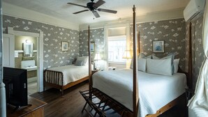 Una cama con dosel, una cama individual más pequeña, un tocador con espejo y un televisor en una habitación de hotel.