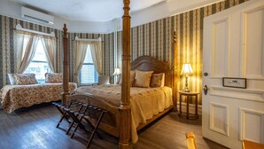 Ein Bett mit Baldachin und einem hölzernen Kopfteil, ein Einzelbett mit blumigem Überwurf sowie ein Nachttisch mit Lampe.