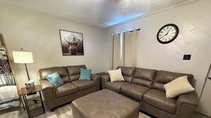 Een woonkamer met twee bruine leren banken, een bijzettafeltje met een lamp, een klok aan de muur en een ingelijste foto.