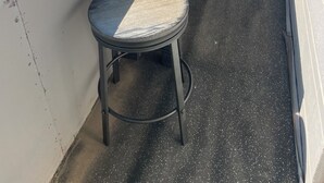 Een balkon met een houten tafel, twee krukken, een metalen emmer en een bord met een reclame voor een winkel in buurt voor huishoudelijke apparaten.