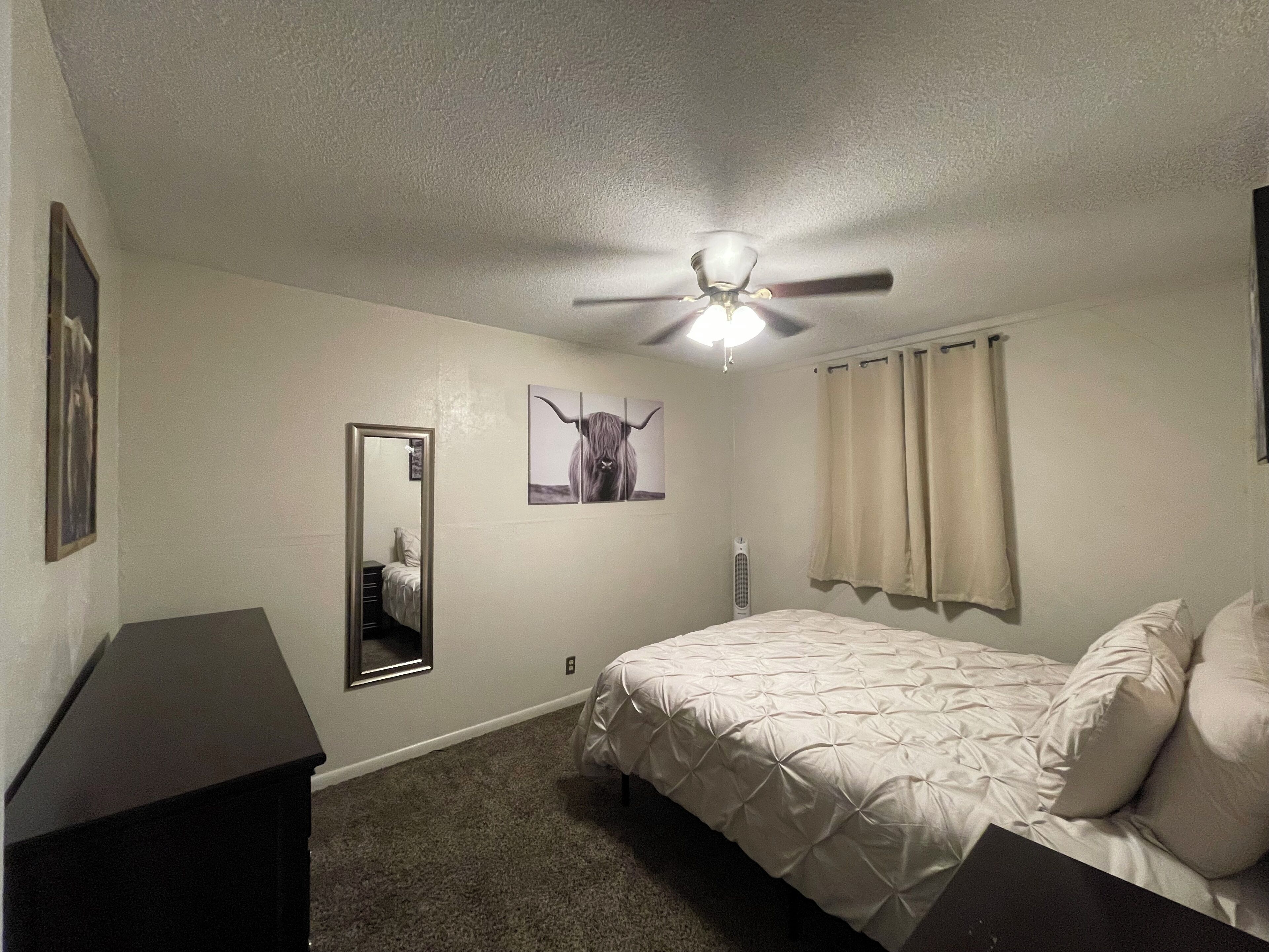 Une chambre à coucher avec un lit, un ventilateur de plafond, un miroir et un tableau représentant un yak.