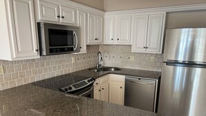 A kitchen with white cabinets, a stainless steel refrigerator, a microwave, a dishwasher, and a granite countertop. - Imagine Waking Up to This View! Relax at the 2 Bedroom Beach Condo in Biloxi, MS (Biloxi)