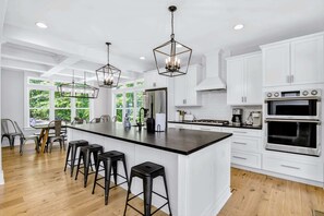A modern kitchen with white cabinets, a large island with bar stools, and pendant lighting. - Lakefront Lake Anna 5 Suites All Water Views (Mineral)