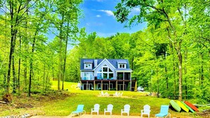A two-story house with a deck, surrounded by a forest.