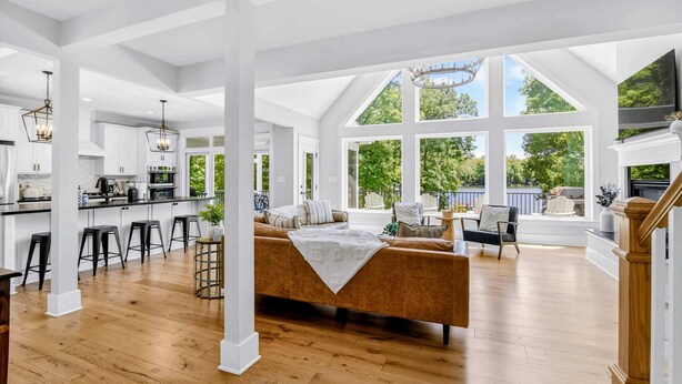 A spacious living area with a large window, a sofa, and a kitchen in the background.